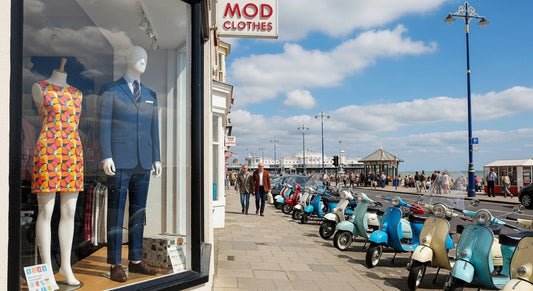 Mod clothes shop in Brighton with tailored suits, mini dresses, and vintage scooters by the seaside.